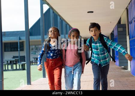 Tre bambini birazziali attraversano un corridoio scolastico con armadietti Foto Stock