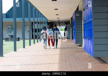 Tre bambini camminano lungo un corridoio scolastico, braccia l'una intorno all'altra, con spazio per le copie Foto Stock