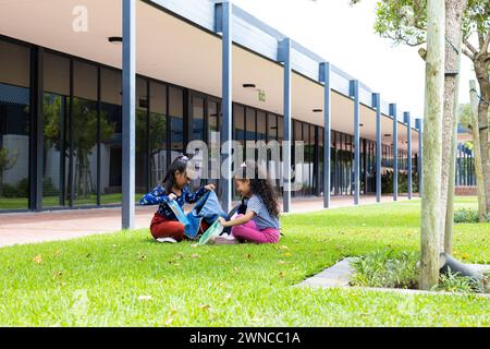 Due ragazze birazziali sono sedute sull'erba a scuola, a pranzare con spazio per le copie Foto Stock