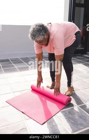 Donna birazziale senior con capelli grigi si avvolge su un tappetino yoga rosa Foto Stock