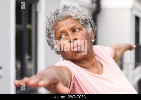 Una donna birazziale anziana con i capelli grigi si allunga le braccia all'aperto Foto Stock