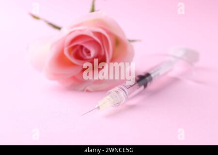 Cosmetologia. Siringa medica e fiore di rosa su sfondo rosa, primo piano Foto Stock