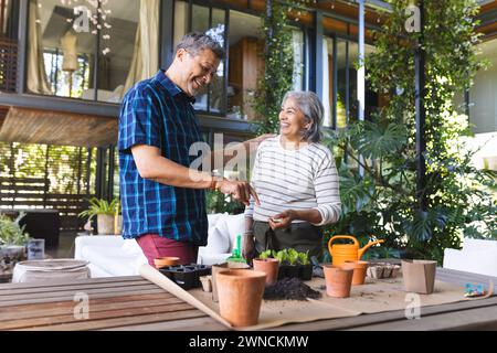 Donna birazziale anziana e uomo birazziale condividono un momento gioioso di giardinaggio insieme Foto Stock