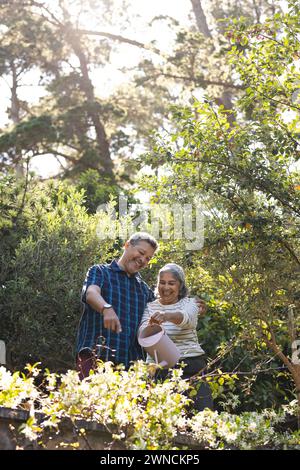 La coppia senior birazziale condivide la gioia nel giardinaggio tra fiori in fiore e luce del sole. Foto Stock