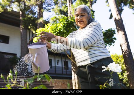 Donna birazziale anziana con capelli grigi che bagna piante in un giardino Foto Stock
