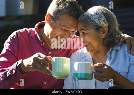 Una coppia birazziale senior condivide un momento di gioia con un brindisi di tazze da caffè Foto Stock