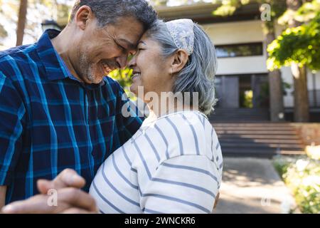 La coppia birazziale senior condivide un momento tenero all'aperto, con sorrisi e sguardi affettuosi Foto Stock
