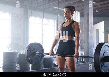 Giovane donna birazziale dalla forma forte solleva un pesante campana in palestra con spazio per fotocopie Foto Stock