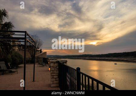 Questa accattivante fotografia cattura la bellezza serena di un tramonto sul lago Travis, con una barca distante che naviga dolcemente attraverso le acque tranquille. T Foto Stock