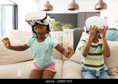 Sorella e fratello afroamericani sono immersi nella realtà virtuale, seduti su un divano Foto Stock