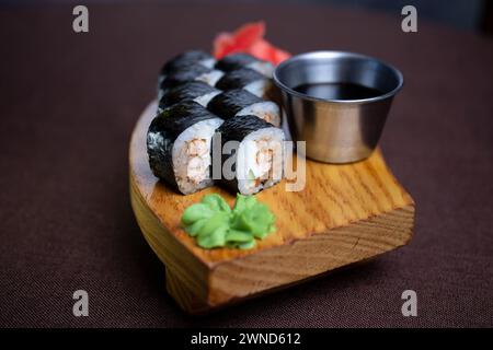 Assortimento di sushi con una varietà di panini e sashimi splendidamente disposti su un piatto di legno, accompagnati da bacchette e un lato di soia saporita Foto Stock