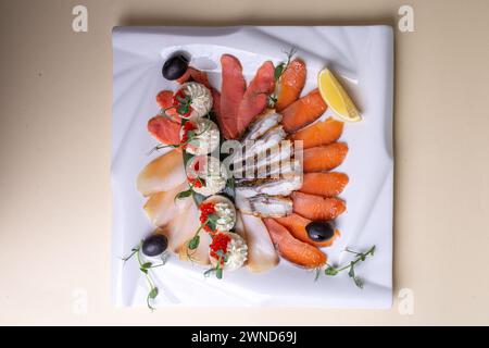 Un piatto di pesce fresco preparato ad arte - salmone, trota, caviale e gamberi - su un piatto bianco con fette di limone e verdure. Un'attrattiva visiva Foto Stock