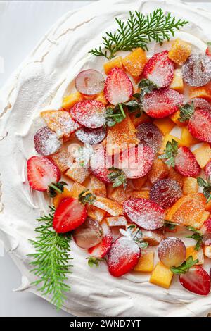 Una torta pavlova bianca adornata con frutti di bosco freschi e un tocco di verde Foto Stock