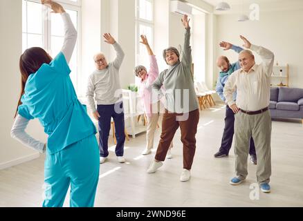 Gruppo di anziani che fanno esercizi di stretching sani per il benessere e la salute con un infermiere. Foto Stock