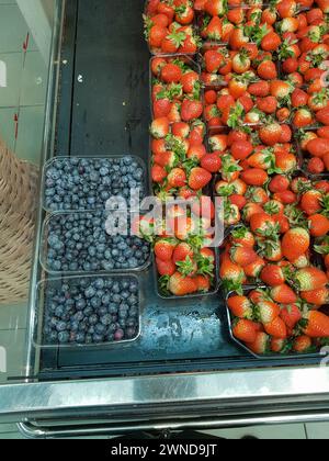 Un sacco di mirtilli e fragole in contenitori sul bancone del negozio, primo piano, verticale Foto Stock