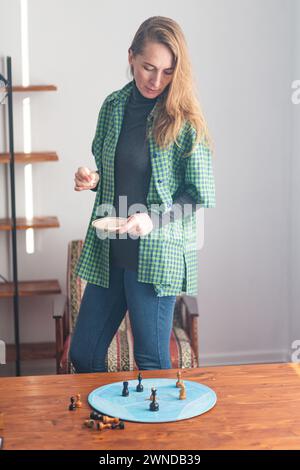 Composizione verticale. Una donna decisa sta accanto al tavolo e guarda con attenzione i pezzi degli scacchi sul cerchio blu. Addestramento psicologico. S Foto Stock