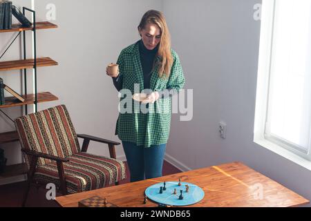 Una donna decisa sta accanto al tavolino e guarda con attenzione i pezzi degli scacchi sul cerchio blu. Addestramento psicologico. Passo dopo passo ana Foto Stock