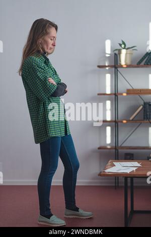 Una donna adulta sta di fronte ad un tavolino su cui ci sono disegni di una casa e pensa. Foto Stock