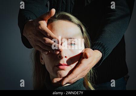 Visualizzazione di un problema psicologico. Difficoltà di comprensione reciproca. Un uomo tiene in mano la testa di una giovane donna adulta, chiudendo una Foto Stock