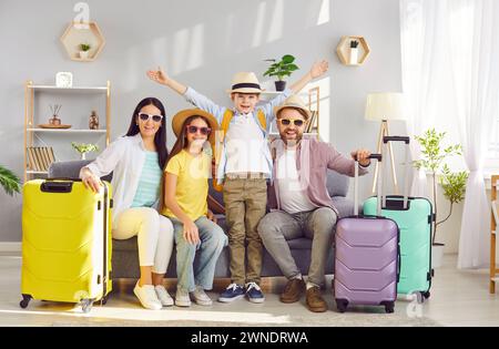 Famiglia felice con bambini seduti sul divano con valigie imballate pronte per le vacanze estive. Foto Stock
