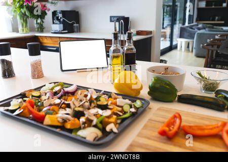 Una varietà di verdure tritate sono pronte su un vassoio, con una compressa e oli da cucina nelle vicinanze Foto Stock