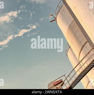 Primo piano, silo e cisterna in un impianto per l'agricoltura, stoccaggio di materiali sfusi e sicurezza dei prodotti con cielo, nuvole ed esterni. Container, struttura agricola e. Foto Stock