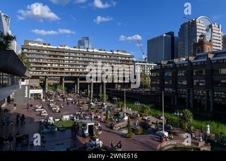 Persone sedute sulla terrazza sul lago di fronte al Barbican Centre. Il Barbican Centre è un rinomato centro artistico e fa parte della Barbican Estate, Foto Stock