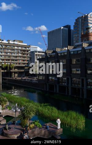 Persone sedute sulla terrazza sul lago di fronte al Barbican Centre. Il Barbican Centre è un rinomato centro artistico e fa parte della Barbican Estate, Foto Stock