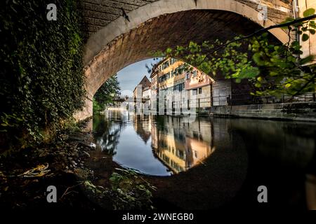 Un tranquillo fiume scorre sotto un ponte, con chiari riflessi degli edifici e degli alberi circostanti, il vecchio porto sul canale con un vecchio mattatoio dentro Foto Stock