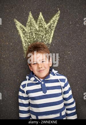 Gesso, ritratto e ragazzo con corona sul pavimento per disegnare, immaginare o fantasia futura su sfondo nero. Re, volto o ragazzo con schizzo di re Foto Stock
