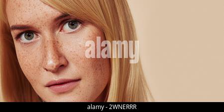 Primo piano di una bella ragazza con una pelle liscia e naturale. Foto in studio ritagliata di donna con lentiggini che guarda la fotocamera sopra il beige B. Foto Stock