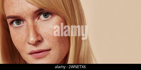 Primo piano di una bella ragazza con una pelle liscia e naturale. Foto in studio ritagliata di donna con lentiggini che guarda la fotocamera sopra il beige B. Foto Stock