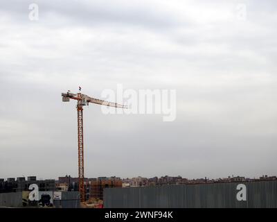 Cairo, Egitto, 23 febbraio 2024: Una torre di gru con la bandiera egiziana che sventolava su di essa, Un sito di costruzione di nuovi edifici residenziali e grattacieli con Foto Stock