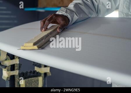 Produzione di tavole da surf, Shaper che lavora sui dettagli della tavola. Concetto di produzione industriale, professionale qualificata, professione e occupazione. Foto Stock