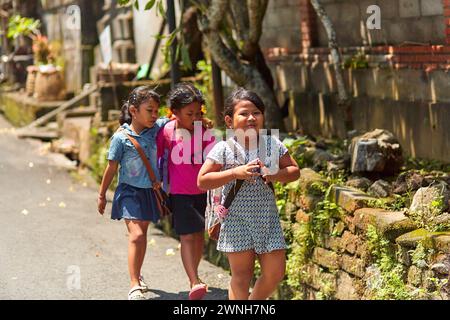 Un gruppo di bambini in uniforme va da scuola lungo una strada in un villaggio indonesiano in Asia. Bali, Indonesia - 03.23.2018 Foto Stock