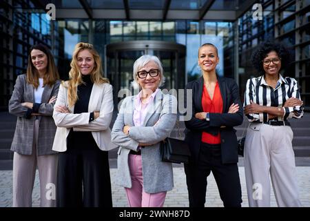 Gruppo di successo di diverse aziende donne formali in piedi con le braccia incrociate che sembrano felici alla telecamera. Foto Stock