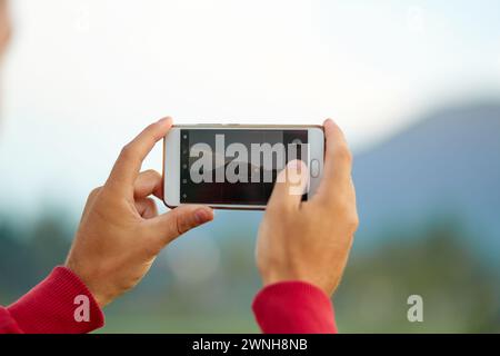 Un giovane uomo si trova sul lato della strada vicino a una risaia e scatta una foto con il suo telefono del Monte Agung sulla famosa isola turistica di Bali Foto Stock