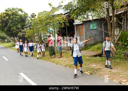 Un gruppo di bambini in uniforme va da scuola lungo una strada in un villaggio indonesiano in Asia. Bali, Indonesia - 03.22.2018 Foto Stock