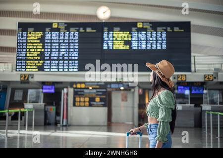 Ragazza ispanica che guarda gli schermi di volo nel terminal dell'aeroporto mentre trasporta il suo spazio per le copie dei bagagli Foto Stock