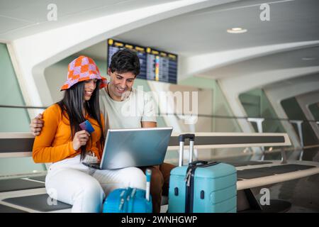 giovane coppia con carta di credito e computer portatile che acquistano il volo all'aeroporto con spazio per le copie dei bagagli Foto Stock