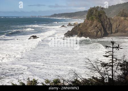 L'oceano è ruvido e le onde si schiantano contro le rocce. Il cielo è limpido e il sole splende Foto Stock