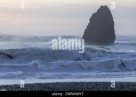 Una grande roccia è nell'oceano, con onde che si infrangono contro di essa. La scena è calma e tranquilla, con la roccia alta e forte contro la forza Foto Stock