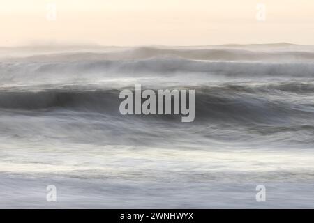 L'immagine è una foto sfocata di un'onda che si schianta su una spiaggia. L'acqua è bianca e il cielo rosa, creando un'atmosfera serena e rilassante. Le onde Foto Stock