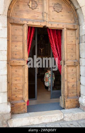 Una donna anziana si inginocchia dietro una porta di legno in una cappella di fronte ad un altare con una figura dorata di Gesù su una croce, Assisi, Umbria, Italia Foto Stock