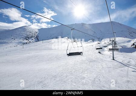 Palo per impianti di risalita con sedie vuote nella località invernale. Giorno di sole, cielo blu. Pendio di montagna. Costruzione di una funivia. Attività per le vacanze invernali. Chunkurchak, Bi Foto Stock