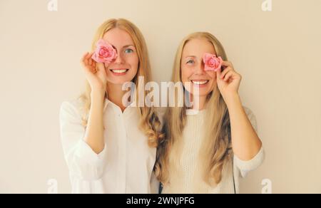 Ritratto estivo di due donne felici sorridenti, madre o sorella di mezza età e figlia adulta con boccioli di rosa rosa sullo sfondo dello studio Foto Stock