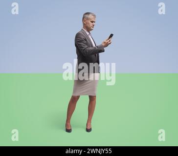 Uomo d'affari aziendale ritratto ritagliato e abbinato a gambe femminili, sta usando uno smartphone, un collage creativo Foto Stock