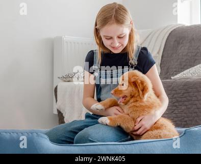 Piccola ragazza con cucciolo Toller siede nel Blue Dog Bed, Nova Scotia Duck Tolling Retriever Foto Stock