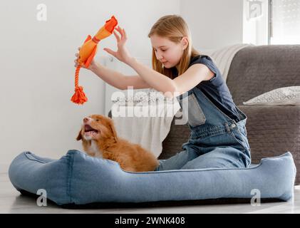 Little Girl gioca con Toller Puppy usando Orange Duck Toy in Dog Bed, Un Retriever per il tolling Duck della nuova Scozia Foto Stock