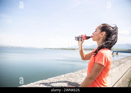 Marzo. 02. 2024 Liptovsky Mikulas. Slovacchia - la donna beve una rinfrescante Coca Cola da una bottiglia di vetro accanto al mare. Foto Stock